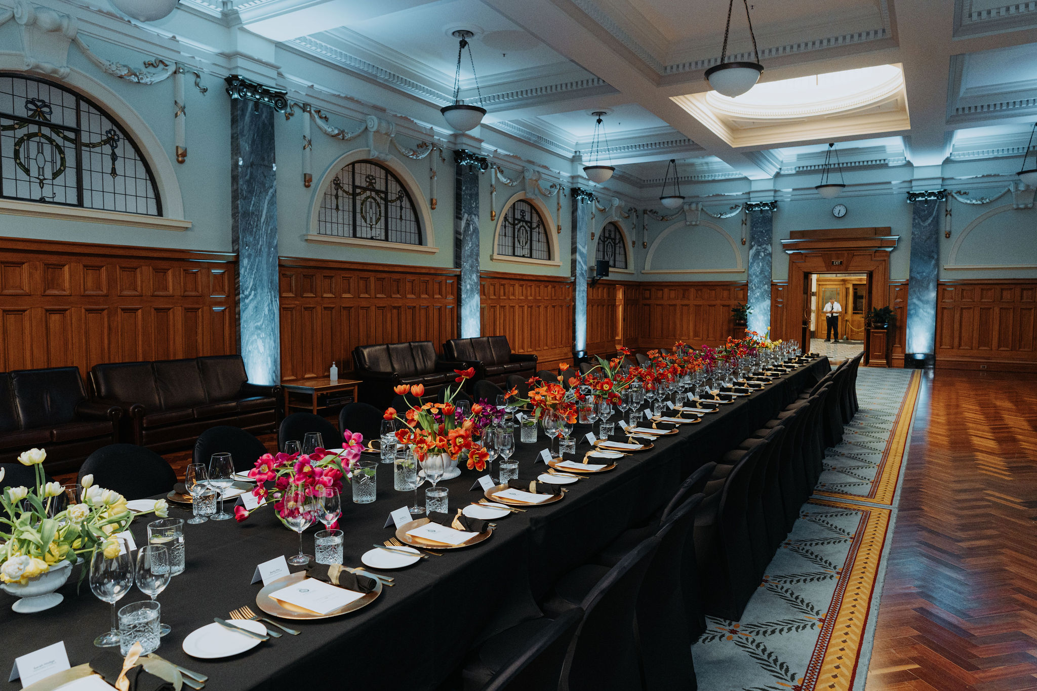 photo of long table setup for dinner in the Grand Hall. Colourful flowers fill the centre of the table.