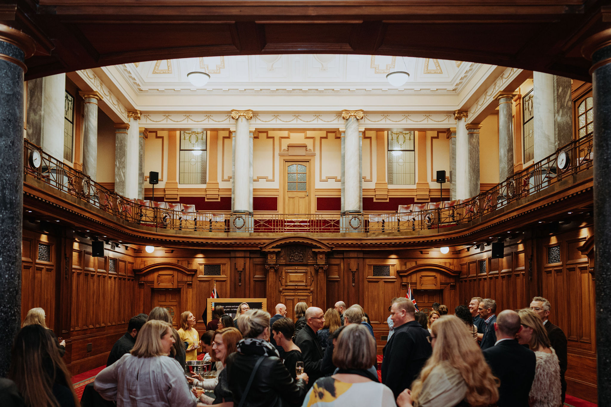 wide photo of Leglislative Council Chamber showing guests standing and talking at an event