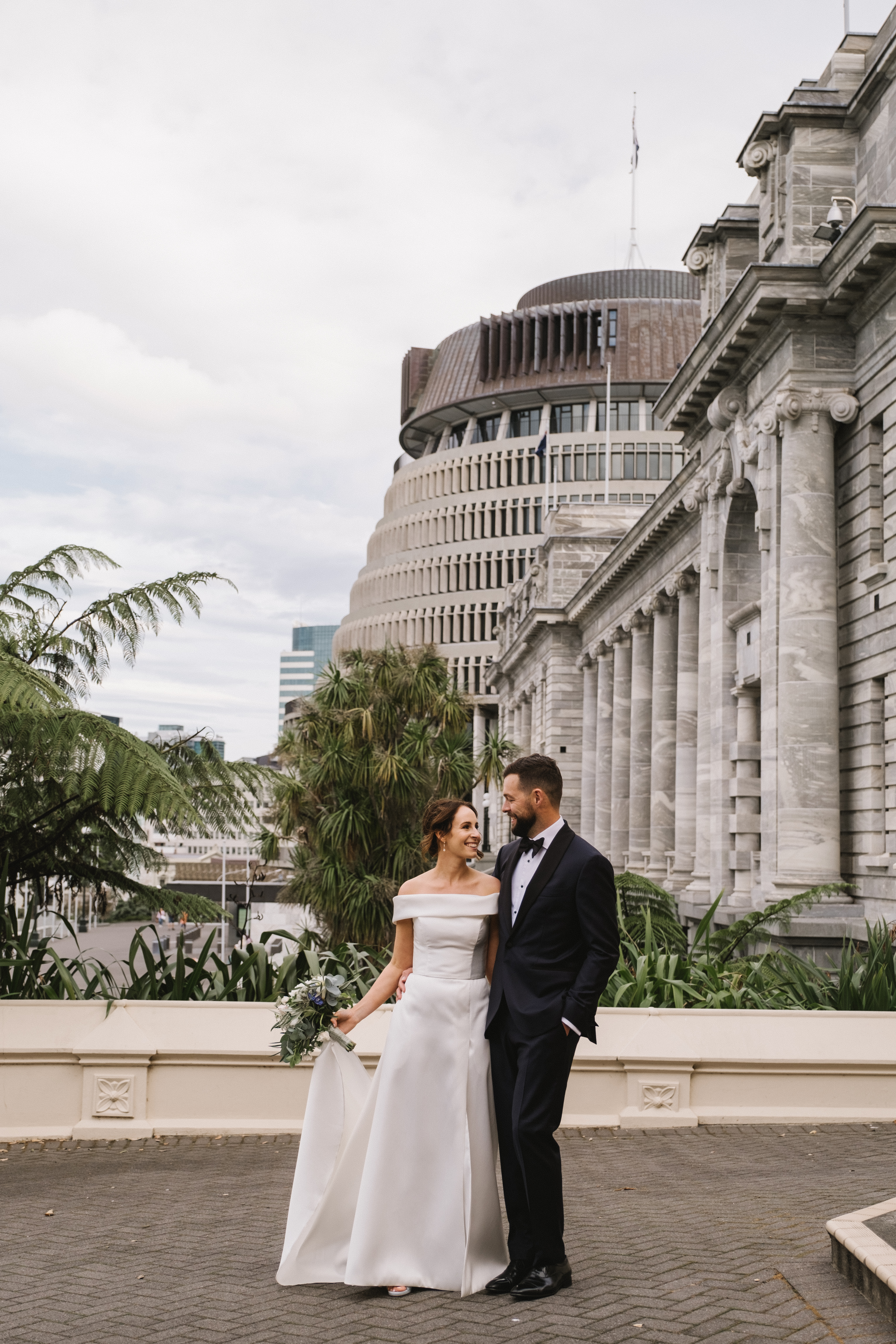 photo of couple dressed in wedding attire standing outside parliament buildings. .