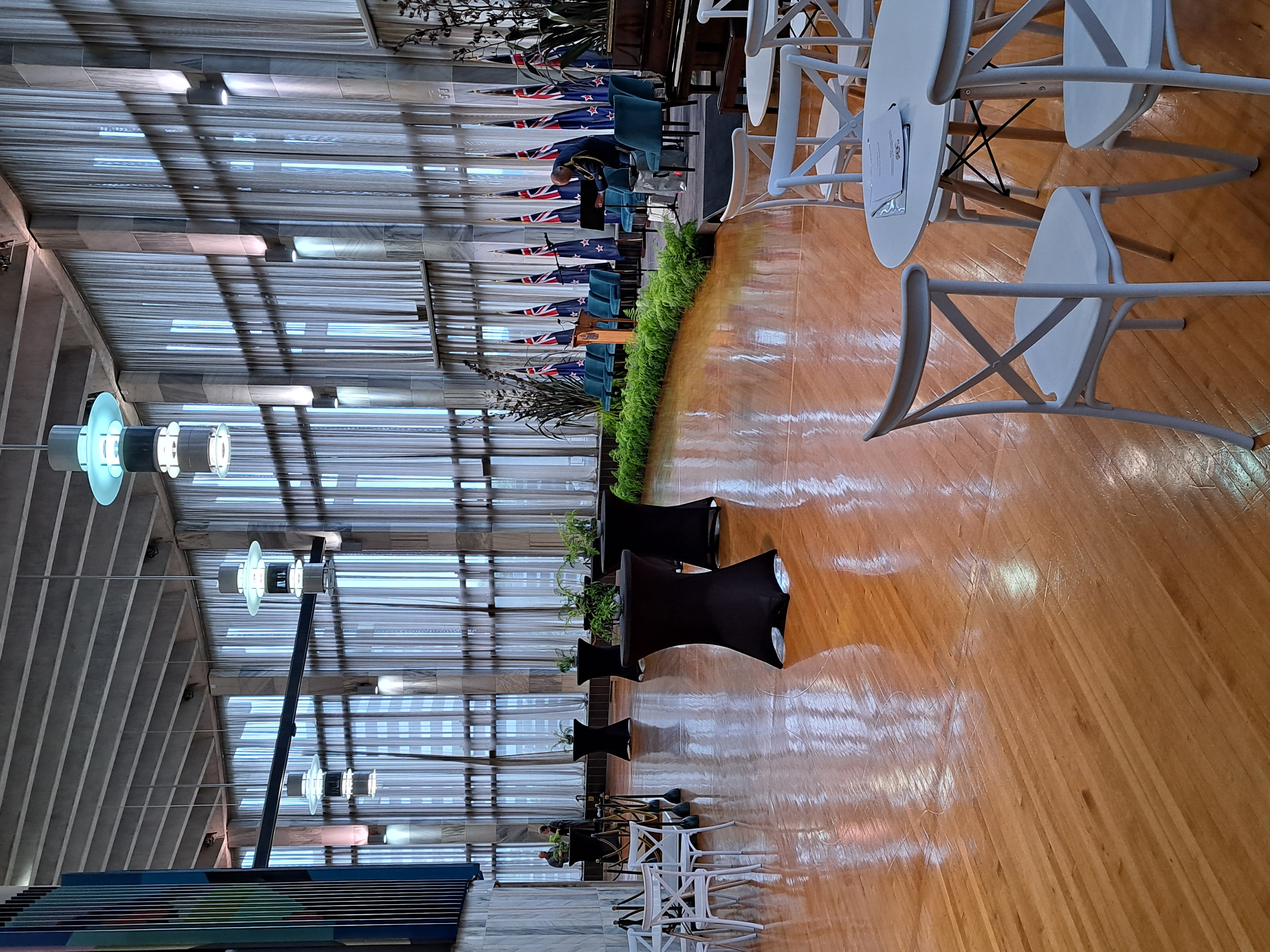 photo of setup for event with stage lined with flags and informal seating and tables spread around hall