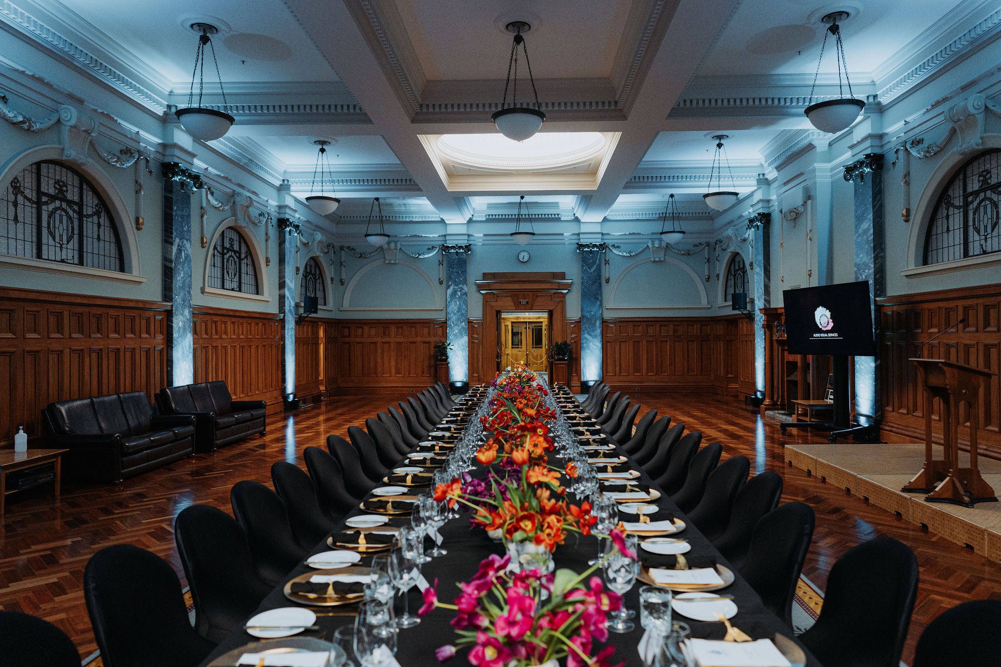 photo of long table setup for dinner in the Grand Hall. Colourful flowers fill the centre of the table.