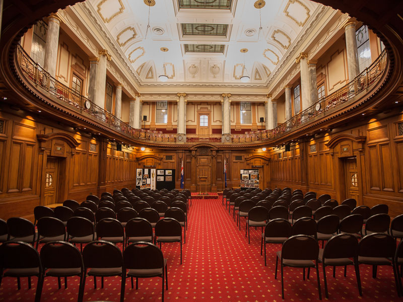 photo of Leglislative Council Chamber setup for event with many empty chairs facing small stage. 