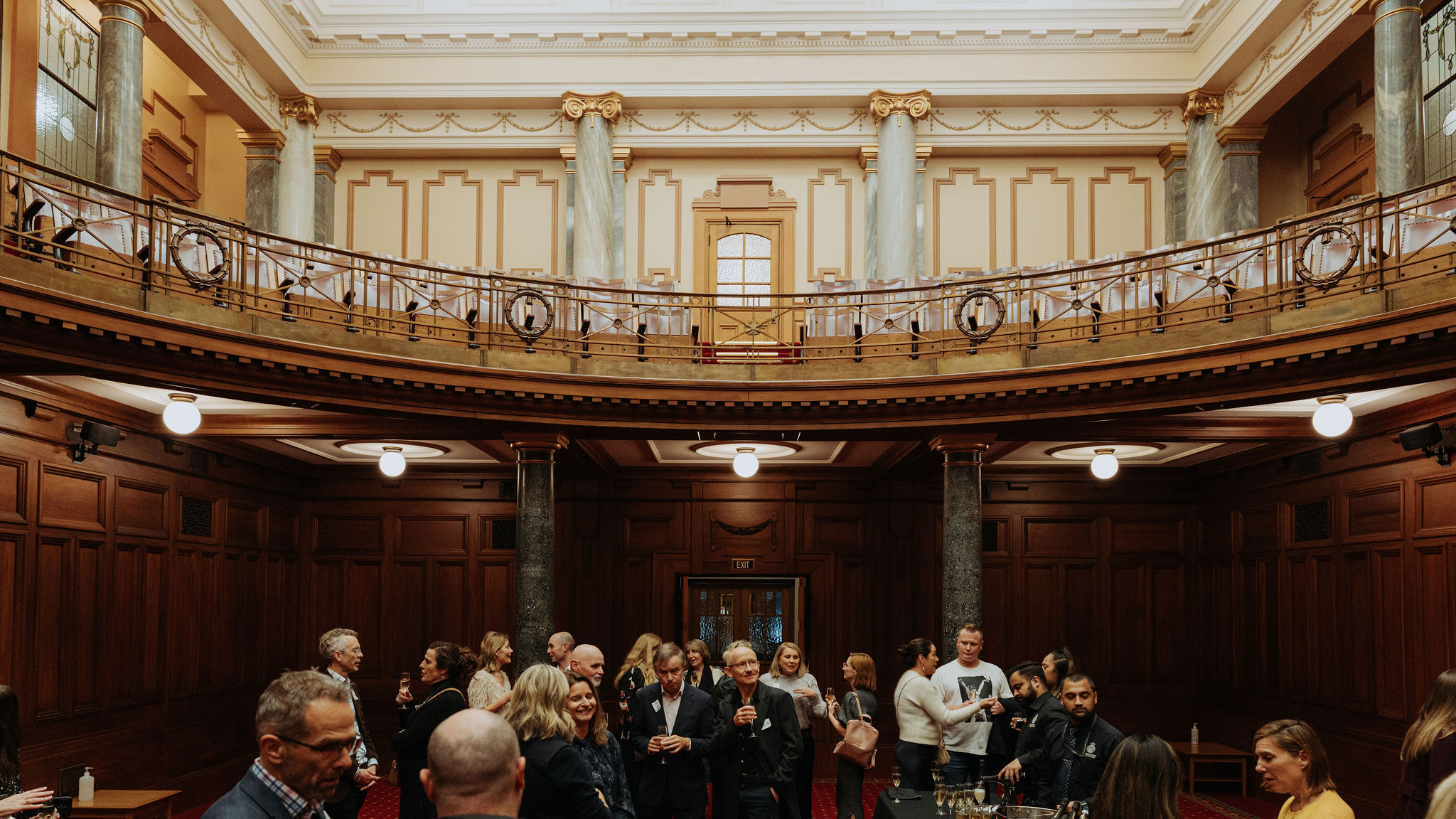 wide photo of Legislative Council Chamber showing guests standing and talking at an event